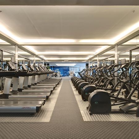 Pathumwan Princess Hotel - Sha Extra Plus Certified Bangkok Exterior photo The photo shows a modern gym space featuring rows of exercise equipment. On one side, there are several treadmills and possibly elliptical machines lined up. The other side has stationary bikes and strength training equipment, arranged neatly. The gy