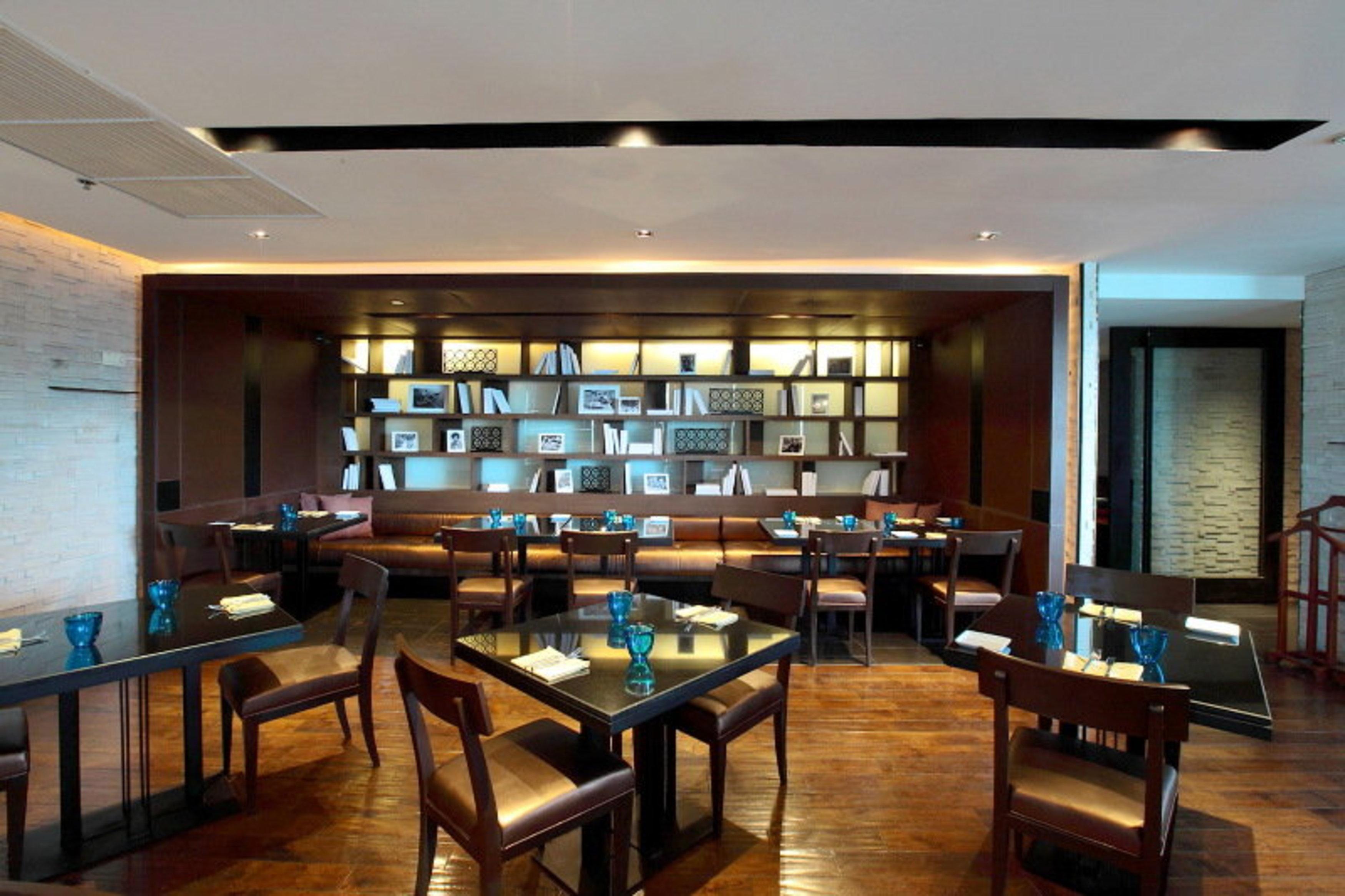 Pathumwan Princess Hotel - Sha Extra Plus Certified Bangkok Exterior photo The photo depicts a modern restaurant interior. It features a warm and inviting atmosphere with wooden flooring and soft lighting. The restaurant has several tables arranged for dining, each set with blue glassware and white napkins. 

On one side, t