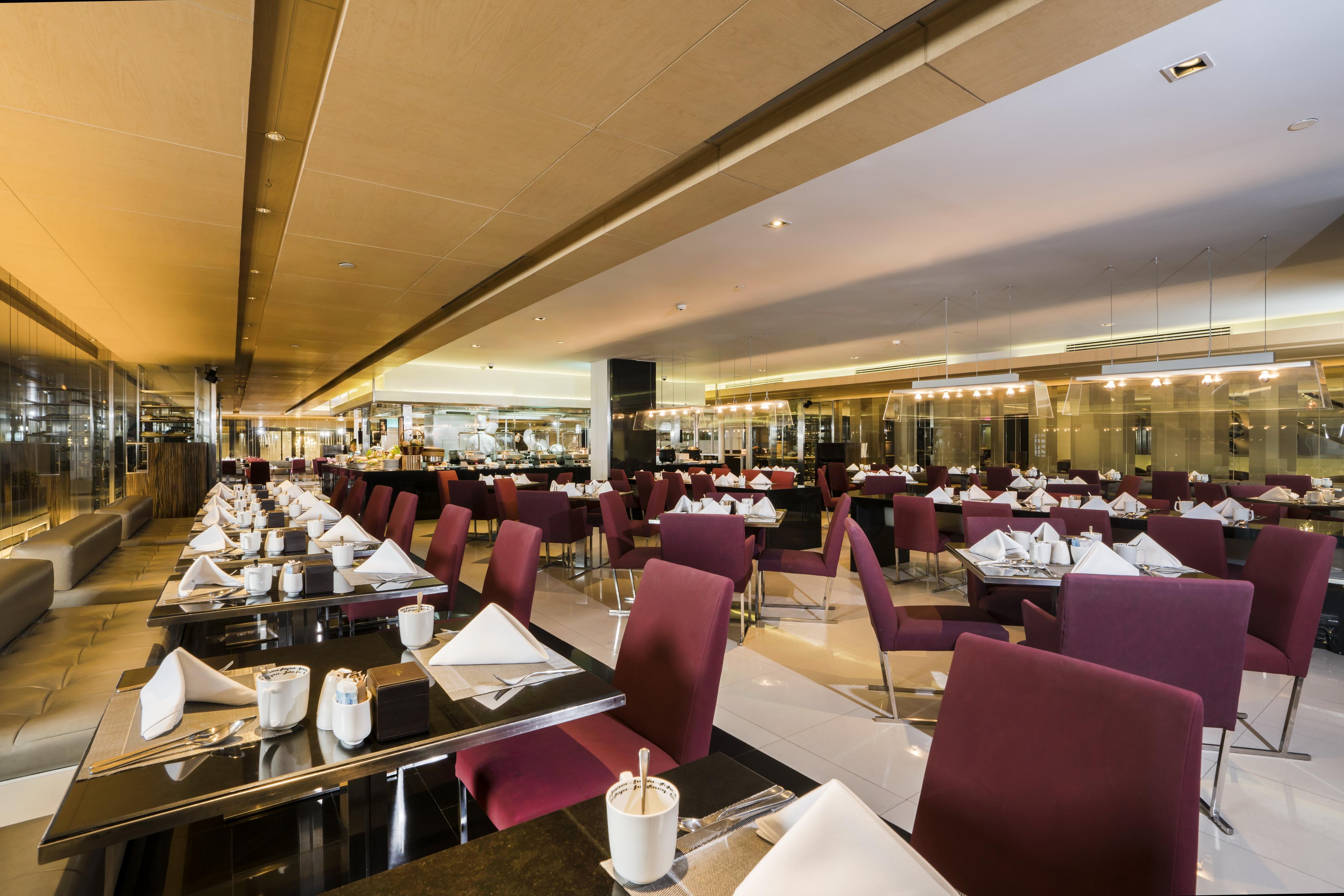 Pathumwan Princess Hotel - Sha Extra Plus Certified Bangkok Exterior photo The image shows a modern restaurant interior. It features a spacious dining area with multiple tables set for guests. The tables are covered with black tablecloths and each one has neatly folded napkins, a small vase, and some utensils. The chairs ar
