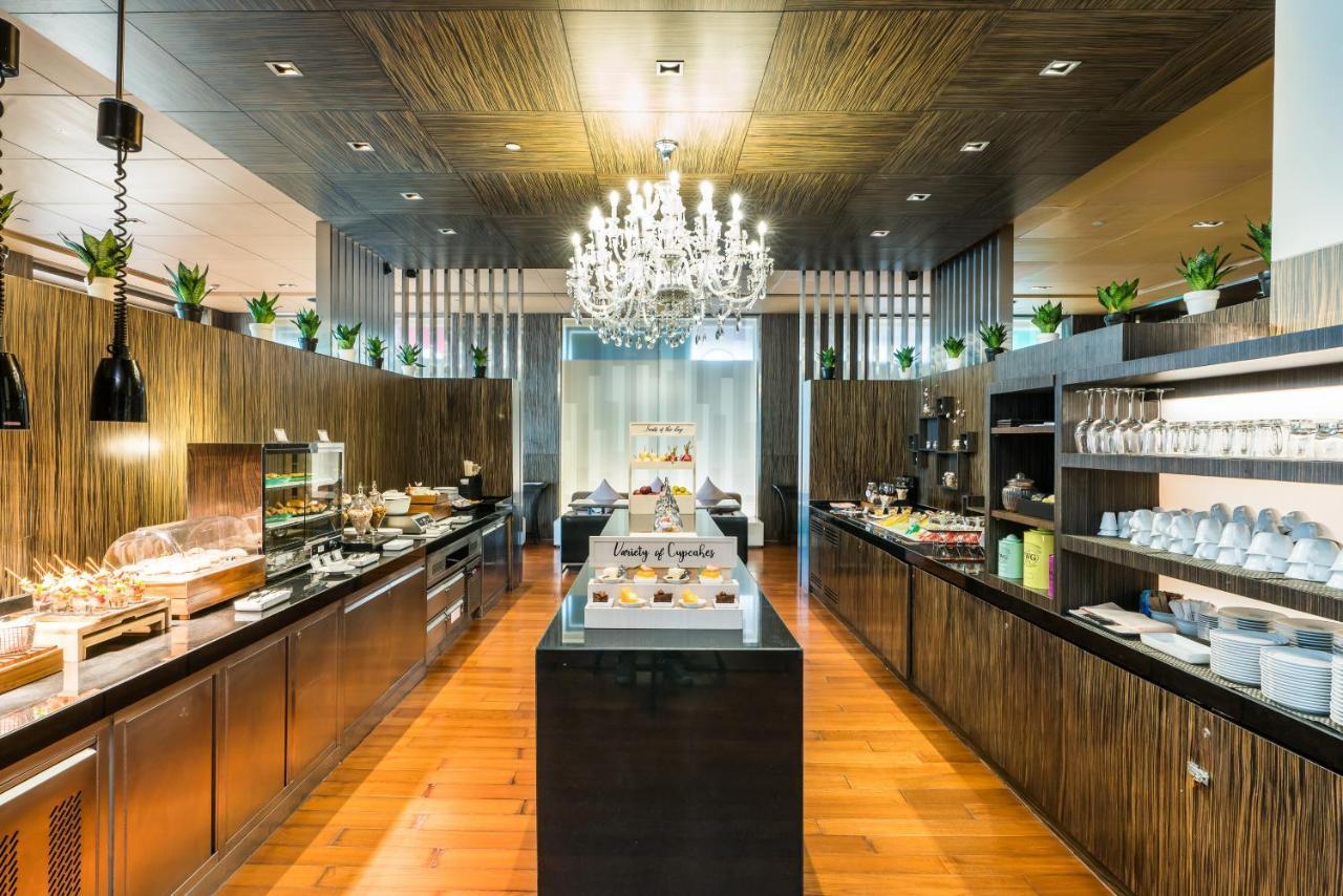 Pathumwan Princess Hotel - Sha Extra Plus Certified Bangkok Exterior photo The photo shows a modern restaurant or buffet area with a stylish interior. The space features wooden walls and flooring, creating a warm ambiance. A large chandelier hangs from the ceiling, adding elegance to the setting. On the right side, there ar