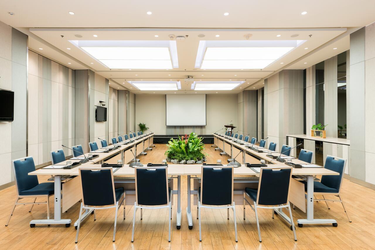 Pathumwan Princess Hotel - Sha Extra Plus Certified Bangkok Exterior photo The photo shows a modern conference room set up for a meeting. The room features a long arrangement of tables with chairs on either side, creating a U-shape. In the center, there is a small planter with greenery. The walls are neutral-toned, and ther